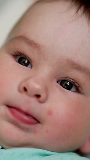 美しい暗い瞳の赤ん坊は平和に背中に横たわっています 舌を示す甘い頬を持つ素敵な子供 クローズアップ バーティカルビデオ — ストック動画