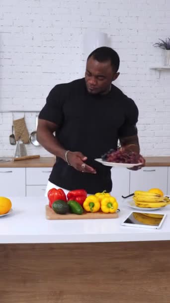 强壮而强壮的非裔美国人看着桌子 桌上有大量的水果和蔬菜 男性运动员在Ipad上查看健康饮食信息 垂直录像 — 图库视频影像