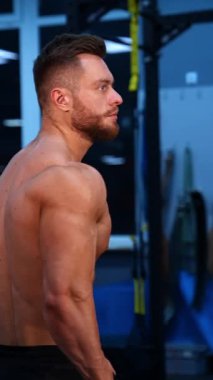 Spor merkezinde güçlü bir atletik adam. Kaslı vücut geliştirici spor salonunda çıplak gövdesini gösteriyor. Atletik vücudu olan yakışıklı, üstsüz bir sporcu. Dikey video