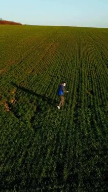 Baharda yeşil alanda koşup duran tatlı bir çocuk. Spor takım elbiseli küçük bir çocuk dışarıda doğal arka planda oynuyor. Hava görünümü Dikey video