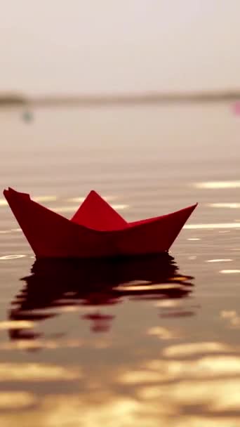 夕阳西下 红纸船独自漂浮 缓慢地在河里漂流 可爱的孩子的折纸船晚上在水面上 特写垂直录像 — 图库视频影像