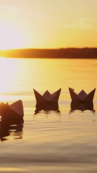 美しい夕日を背景に川に浮かぶ多くの素敵な自家製のペーパーボート 夕方の垂直ビデオで水面に泳ぐ紙から作られた船 — ストック動画