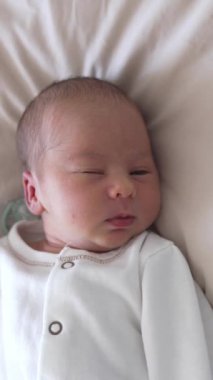 Tatlı bebek yavaşça uykuya dalıyor. Gözlerini kırpıyor ve biraz gülümsüyor. Uykucu tatlı çocuk, yukarıdan bak. Dikey video