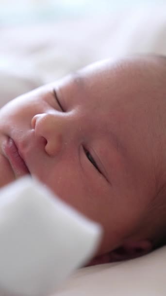 小さな子供はゆっくりと目をそらして 徐々に眠りにつきます 白いベッドの上の白い服の甘い赤ん坊 美しい赤ちゃんの顔が近づいています バーティカルビデオ — ストック動画