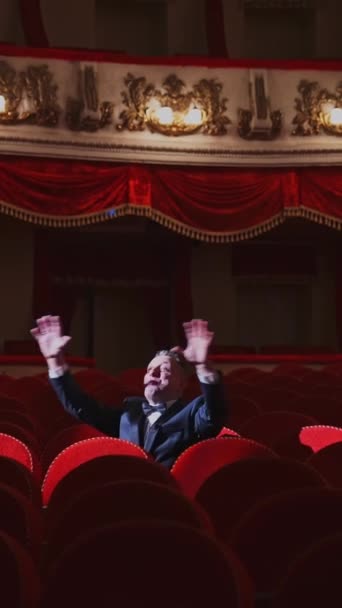大きな講堂で一人でスーツを着た成功した男 俳優は空っぽの赤いアームチェアの中に座り オペラハウスで歌っている バーティカルビデオ — ストック動画