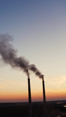 Akşamları doğada boruları olan bir fabrika. Kara dumanlı iki endüstriyel boru gün batımında çevreyi kirletiyor. Dikey video