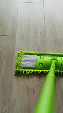 Yerleri su ve bezle temizliyorum. Yeşil kovanın yanındaki parke zemininde suyla hareket eden yeşil paspas. Günlük rutin işler. Hijyen konsepti. Dikey video