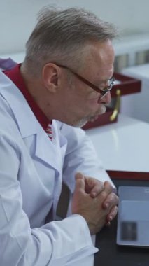 Profesyonel doktor bir hastayla çevrimiçi konuşuyor. Gözlüklü kendine güvenen doktor hastane ofisinde bilgisayarını uzaktan kullanan bir hastaya danışıyor. Uzaktan başvuru işi. Dikey video