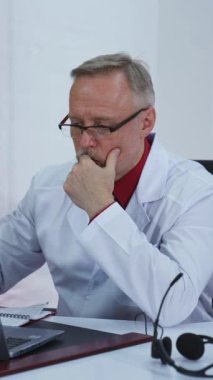 Doktor görüntülü aramaya başlıyor. Tıp merkezindeki uzaktan muayene sırasında kulaklık takan profesyonel bir doktor. Karantina sırasındaki uzak ilaçlar. Dikey video