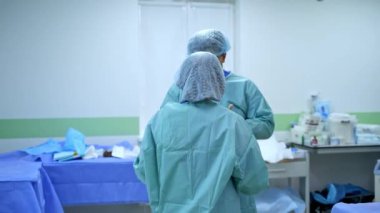Erkek cerrah ameliyat için hazır. Kadın hemşire, doktorun bornozu bağlamasına yardım ediyor..