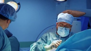 Cerrah travma tedavi operasyonunda metal forseps kullanır. Tıbbi ekip ameliyathanede aydınlatma altında çalışıyor..