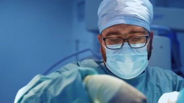 Travma ameliyatı yapan gözlüklü ve maskeli bir doktor. İş yerindeki bir profesyonelin portresini kapat..