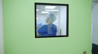 Erkek doktor ameliyathanenin kapısında bekliyor. Pencere ve cerrah olan bir kapıyla aradaki mesafe.