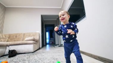 Odanın etrafında koşan mutlu gülen çocuk. Bebek kanepeye gider kediye basar ve onu korkutur. Düşük açı görünümü.