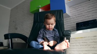 Rahat bir ofiste elinde uzaktan kumandayla oturan Kafkasyalı çocuk. Tatlı çocuk başka tarafa bakıyor ve kameraya sevimli bir şekilde gülümsüyor. Düşük açı görünümü kapat.