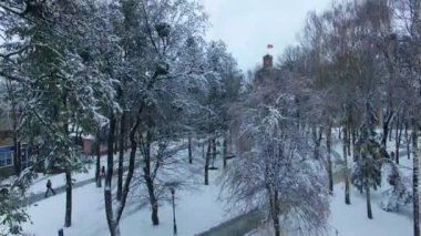 Kış mevsiminde, saati olan eski kuleyle park et. Gündüz vakti karlı şehir panoramasında İHA yükseliyor. Üst görünüm.
