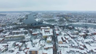 Nehir ve köprüsü olan bir panorama. Karlı kış gündüz insansız hava aracı görüntüleri. Şehir manzarası sisli ufukta.