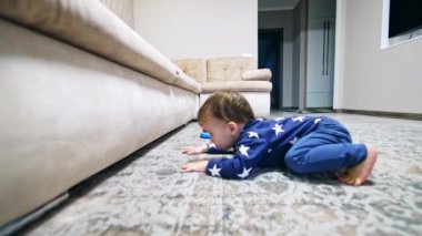 Komik çocuk kanepenin altına bakmak için yere düşüyor. Güzel çocuk oyuncağı mobilyaların altından almaya çalışıyor..