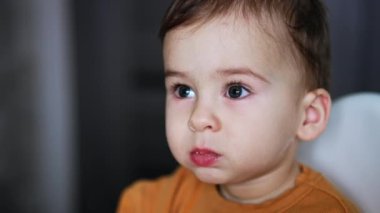 Beslenme sırasında bir yaşında, beyaz bir çocuğun yüzü vardı. Çocuk dikkatlice yana bakıyor ve sonra elini ağzına alıyor. Kapat..