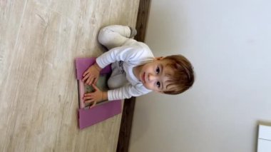 Yerde pullarla oynayan sevimli bir bebek. Sevimli küçük çocuk ağırlıklarda oturur ve kameraya bakar. Dikey video.