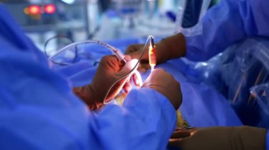 Cerrahın eldivenli eli farların ışığında aletlerle çalışıyor. Diğer doktor destek aletleri. Kapat..