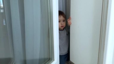 Sevimli beyaz oğlan balkon kapısını açıyor ve gülümsüyor. Öndeki kara kedi..