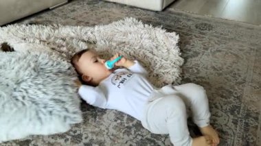 Beyaz tişörtlü sevimli erkek bebek ağzında emzik ile yerde yatıyor. Çocuk yumuşak yumuşak bir yastıkla sarılır. Üst görünüm.