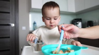 Kafkas bebeği annesi tarafından kaşıkla ve tabakla besleniyor. Çocuk kaşığını aldı ve biraz yemek toplamaya çalıştı..