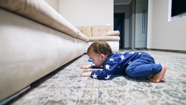 有趣的孩子倒在地板上看沙发下面 可爱的小孩想把玩具从家具下面拿出来 — 图库视频影像