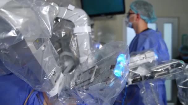 手術中に動くロボットアームを完全に覆った マスクとメガネの男性の薬はぼやけの背景に立っています — ストック動画