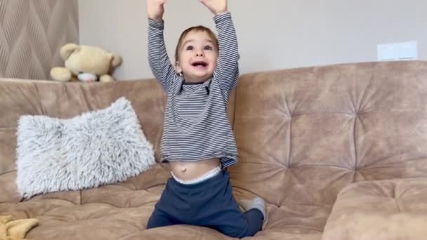Счастливого Приветственного Мальчика Сидящего Диване Милый Ребенок Прыгает Улыбается Размахивает — стоковое видео