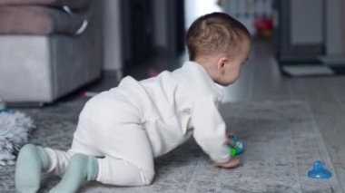 Bir yaşındaki çocuk oyuncaklarla oynuyor. Çocuk yerde sürünüyor, küçük bir arabayı hareket ettiriyor. Bulanık arkaplan.