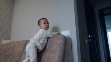 Aktif çocuk kanepede yürür ve elektrik düğmesine ulaşır. Odadaki aydınlatma düğmelerini açıyor. Düşük açı görünümü.
