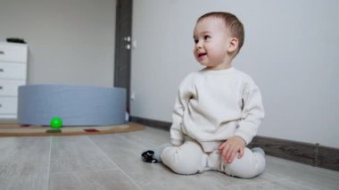 Beyaz takım elbiseli, gülümseyen çocuk yerde oturuyor. Bebek bir an için düşünür ve sonra sürünerek uzaklaşır..