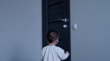 Küçük çocuk ışık düğmesine doğru yürüyor. Bebek sevinçle tezahüratın ve gülümsemenin ışığını açıyor..