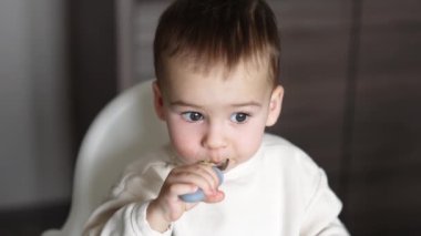Güzel beyaz erkek bebek çocuklar için özel bir kaşıktan kendini yiyor. Kapatın. Yüksek açı. Bulanık arkaplan.
