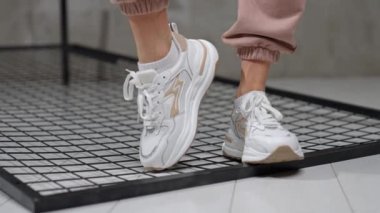 Bej desenli beyaz spor ayakkabılar. Model stüdyodaki metal ızgaranın yanından geçiyor. Kapat..