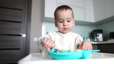 Küçük çocuk kaşıkla tabaktan yemek yiyor. Bebek büyüyor, gelişiyor ve öğreniyor.