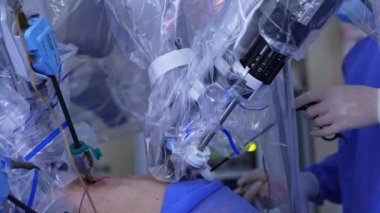Robot manipülatör kollar laparoskopik prosedürü gerçekleştirir. Yanında duran doktor tıbbi aletler kullanıyor. Kapat..