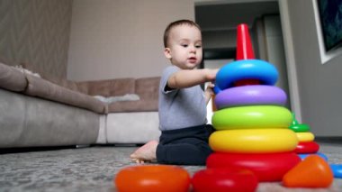Tatlı çocuk piramit halkalarını yerden alıyor. Yürüyen çocuk piramit inşa eder ve boyut ve renkleri öğrenir. Düşük açı görünümü.