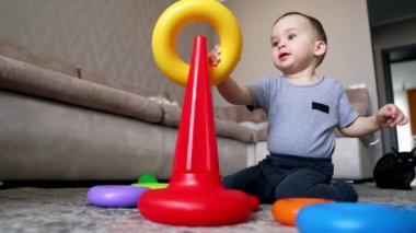 Güzel beyaz çocuk piramit inşa ediyor. Mutlu erkek bebek evde oynuyor. Kara kedi arka planda. Düşük açı görünümü.