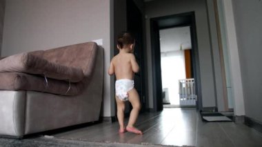 Evde koşuşturan sevimli, mutlu beyaz çocuk. Bezli bebek evde oynuyor. Düşük açı görünümü.