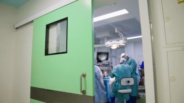 Koridorun sonundaki açık kapıdan ameliyathaneye bakın. Cerrah ameliyat masasında sandalyeye oturur..