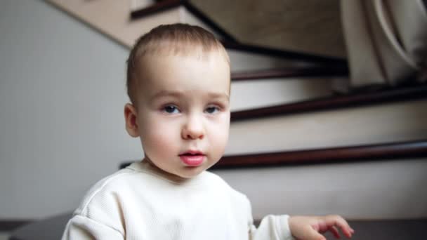 小男孩竭力想把他的袜子脱下 可爱的孩子坐在楼梯上看着摄像机 靠近点 — 图库视频影像