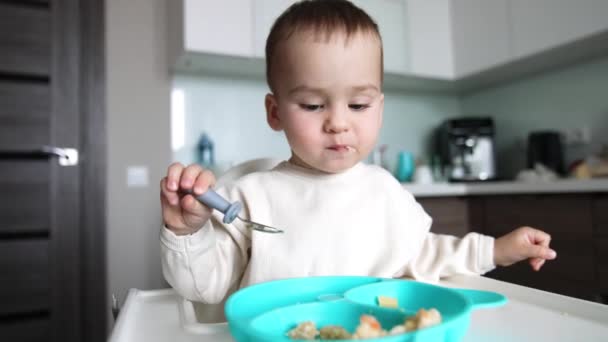 一个可爱的小孩的晚餐时间 婴儿坐在餐桌上用勺子吃饭 靠近点模糊的背景 — 图库视频影像