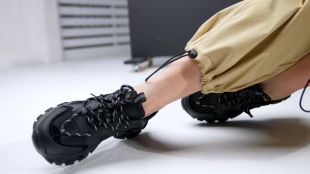 黑色时髦的大块头女足运动鞋 穿着米色宽裤子的女人坐在地板上展示她的运动鞋 — 图库视频影像