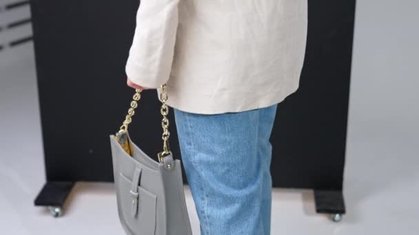 女性の手の金の鎖のハンドルが付いている美しい灰色の革袋 現代のハンドバッグを保持するジャケットとジーンズの女性 — ストック動画