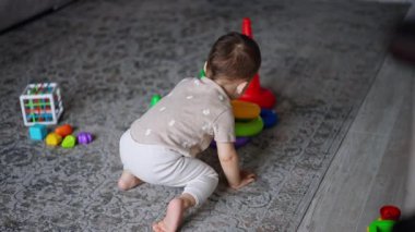 Tatlı küçük oğlan yerde oyuncaklarla oynuyor. Güzel bebek piramidi birleştiriyor ve merdivenlerden sürünerek çıkıyor..