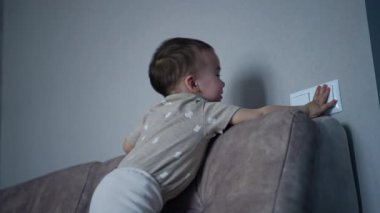 Mutlu yürümeye başlayan çocuk ışığı açar. Erkek bebek heyecanlı bir şekilde tavanı işaret ediyor. Düşük açı görünümü.