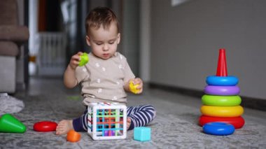 Ciddi bebek halının üzerinde oturan oyuncaklarla oynuyor. Küçük çocuk evde huzur içinde oynuyor..
